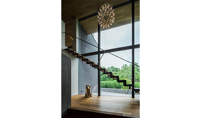 階段ホールよりテラス越しに中庭を望む。隣地の雑草が視界に入らぬ様、庭には蛇籠を巡らせた。