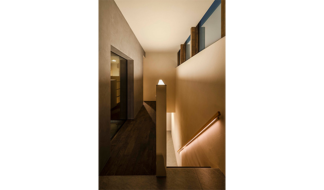 2階階段ホール夕景。階段脇のハーフウォールと手摺に間接照明を仕込み、階段とホールの全体照明としている。