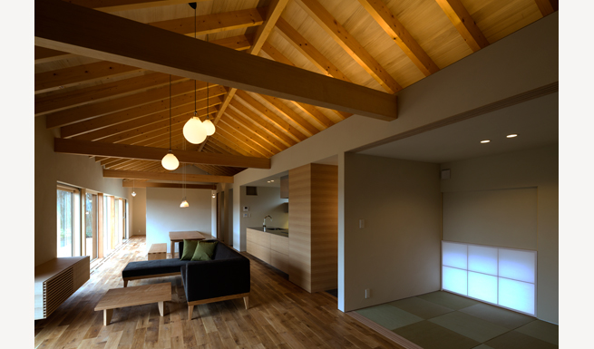TATAMI ROOM、キッチン、水廻りの上がロフトとなっている。垂木が美しくライトアップされた室内。